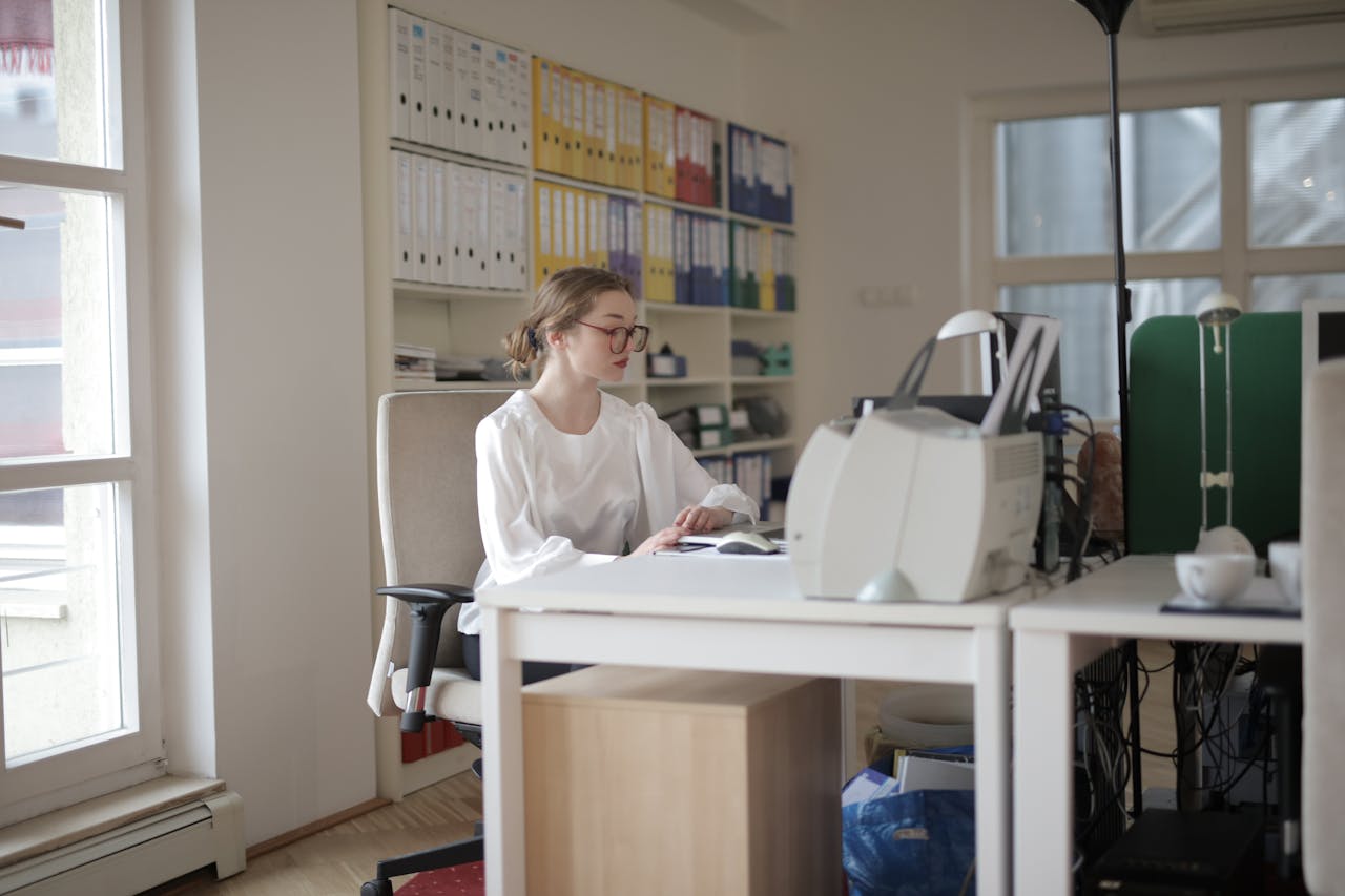 services-img-02 Focused woman working in a modern office filled with files and equipment.