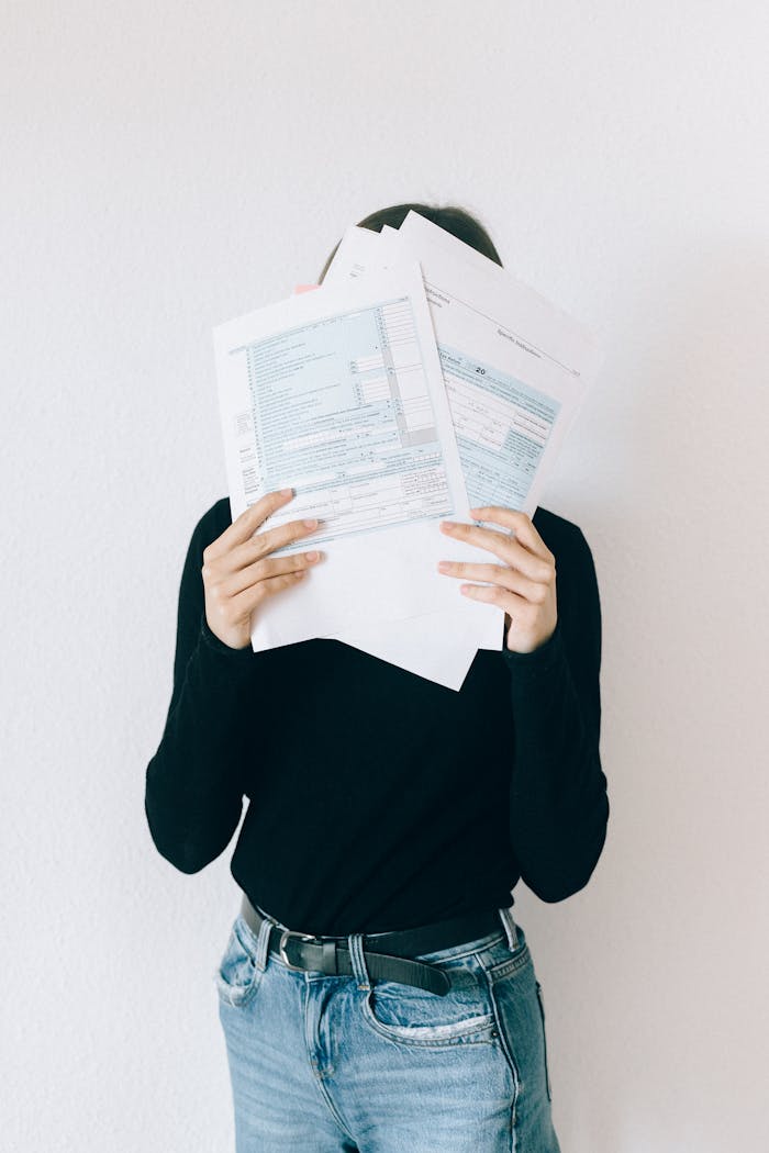 about-img-02 A woman concealing her face with tax forms, illustrating financial stress and paperwork burden.