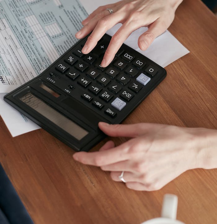 services-03 Person calculating finances with a calculator and document on a wooden desk.